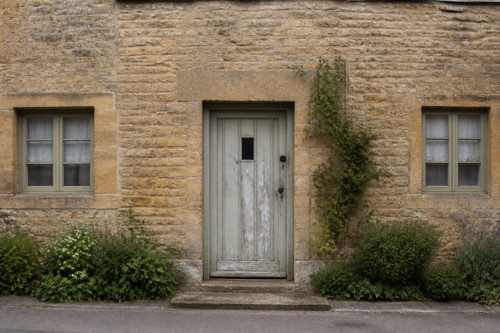 A honey-coloured stone cottage with a weathered peeling painted timber front door.
