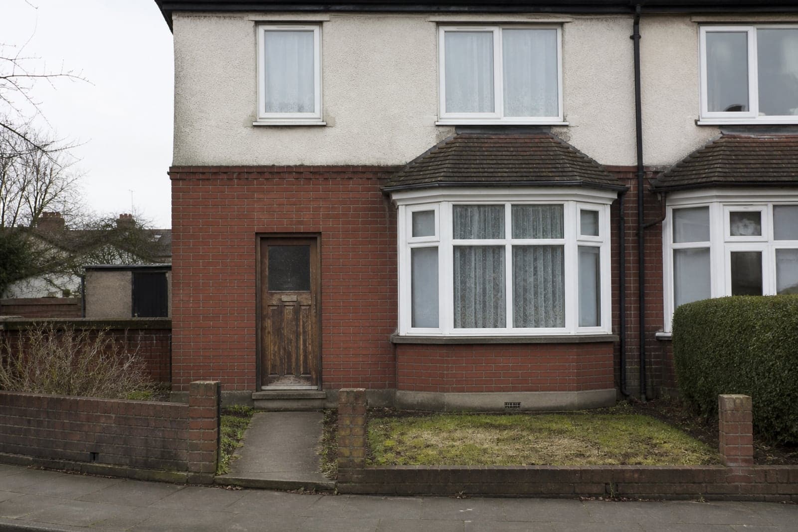 A 1930s semi-detached house with a bay window and an old flaking stained-timber front door.